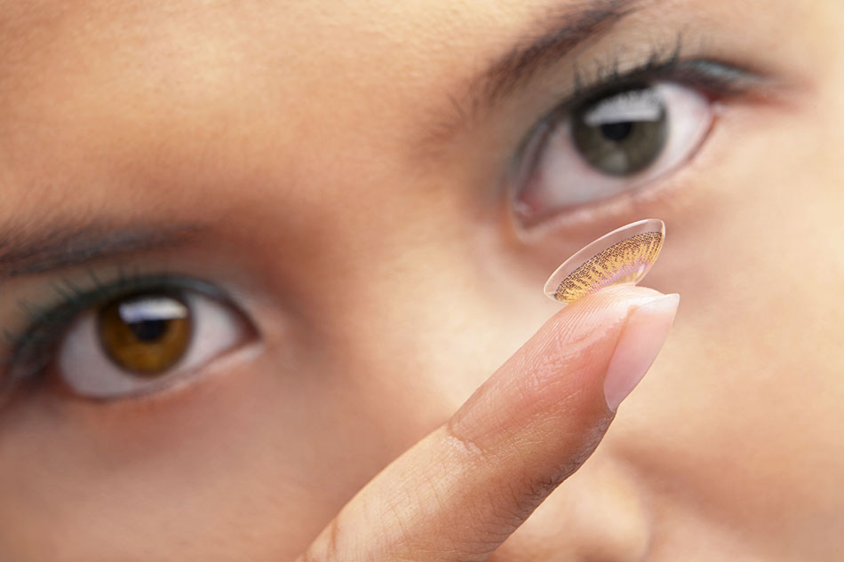 Woman with two different eye colors holding a color contact lens on her finger